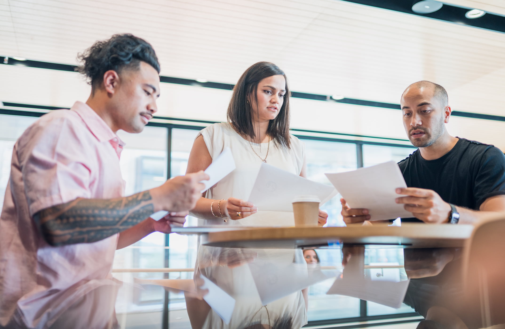 Three people hold papers as they meet in a professional environment.