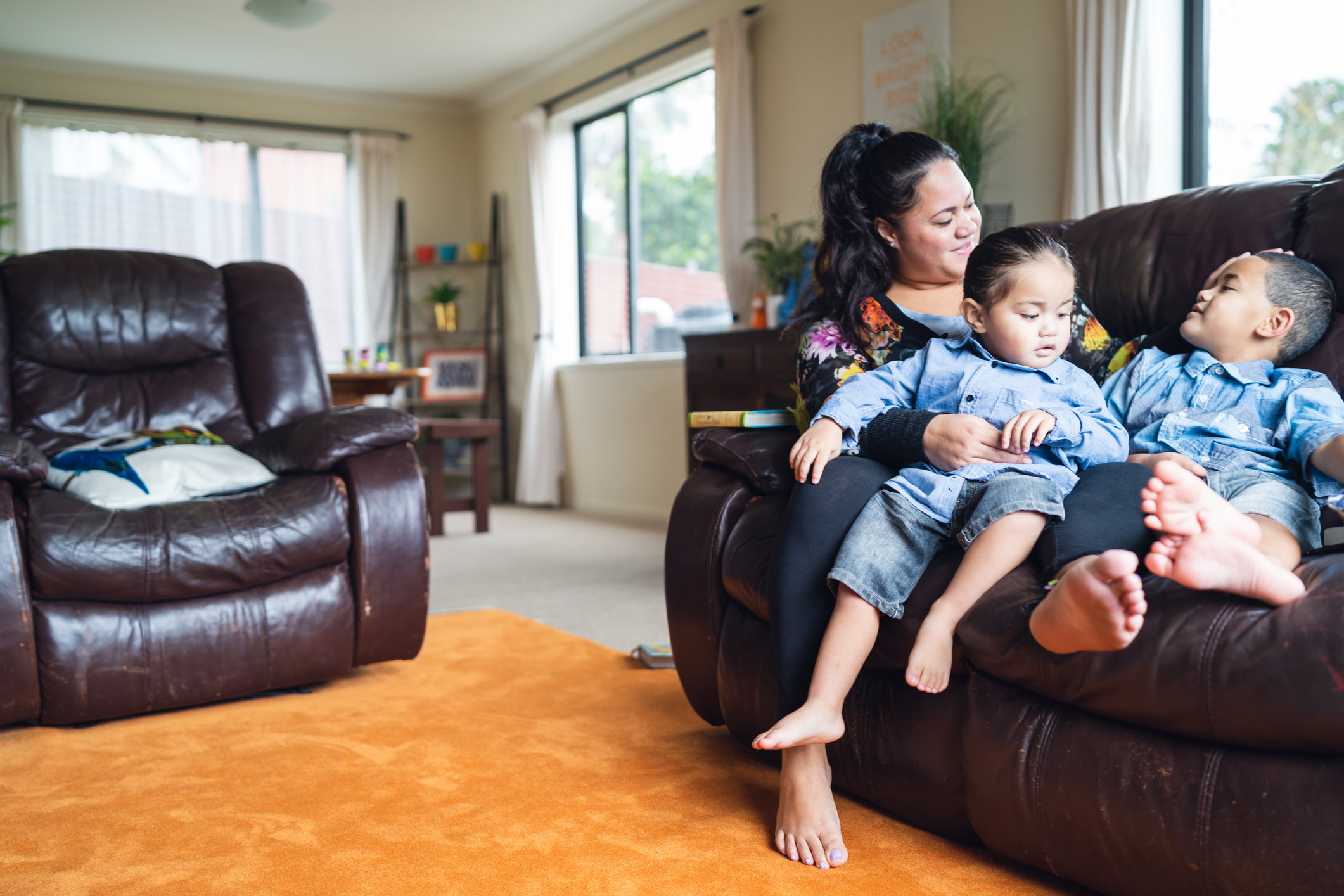 A mother sits on the couch with her two young children.