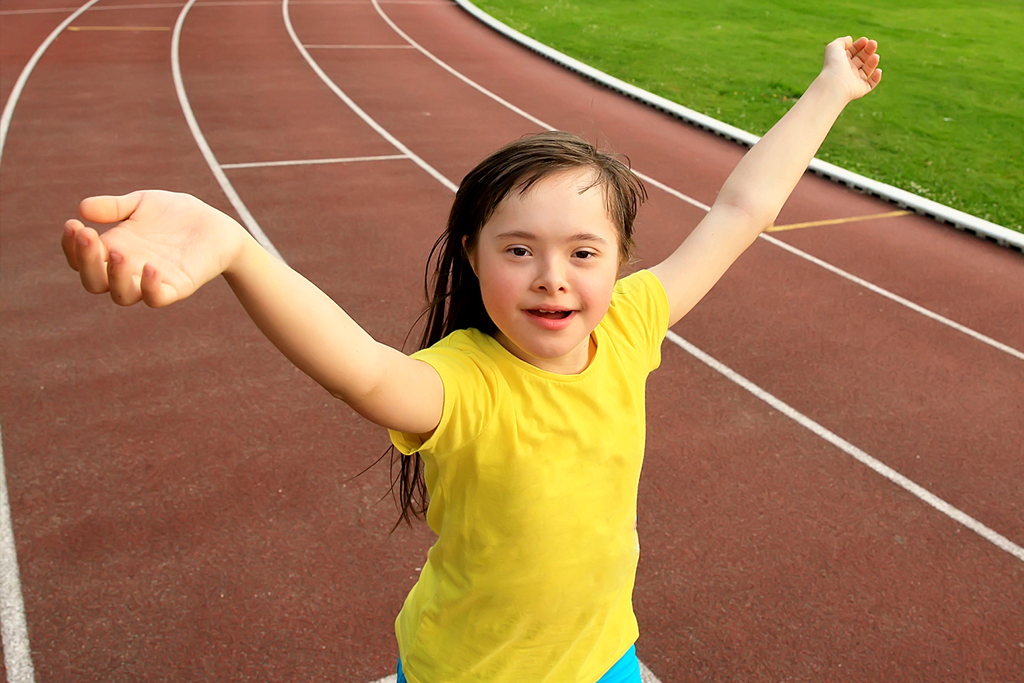 A Down Syndrome girl with arms raised crosses the finish line on a race track.