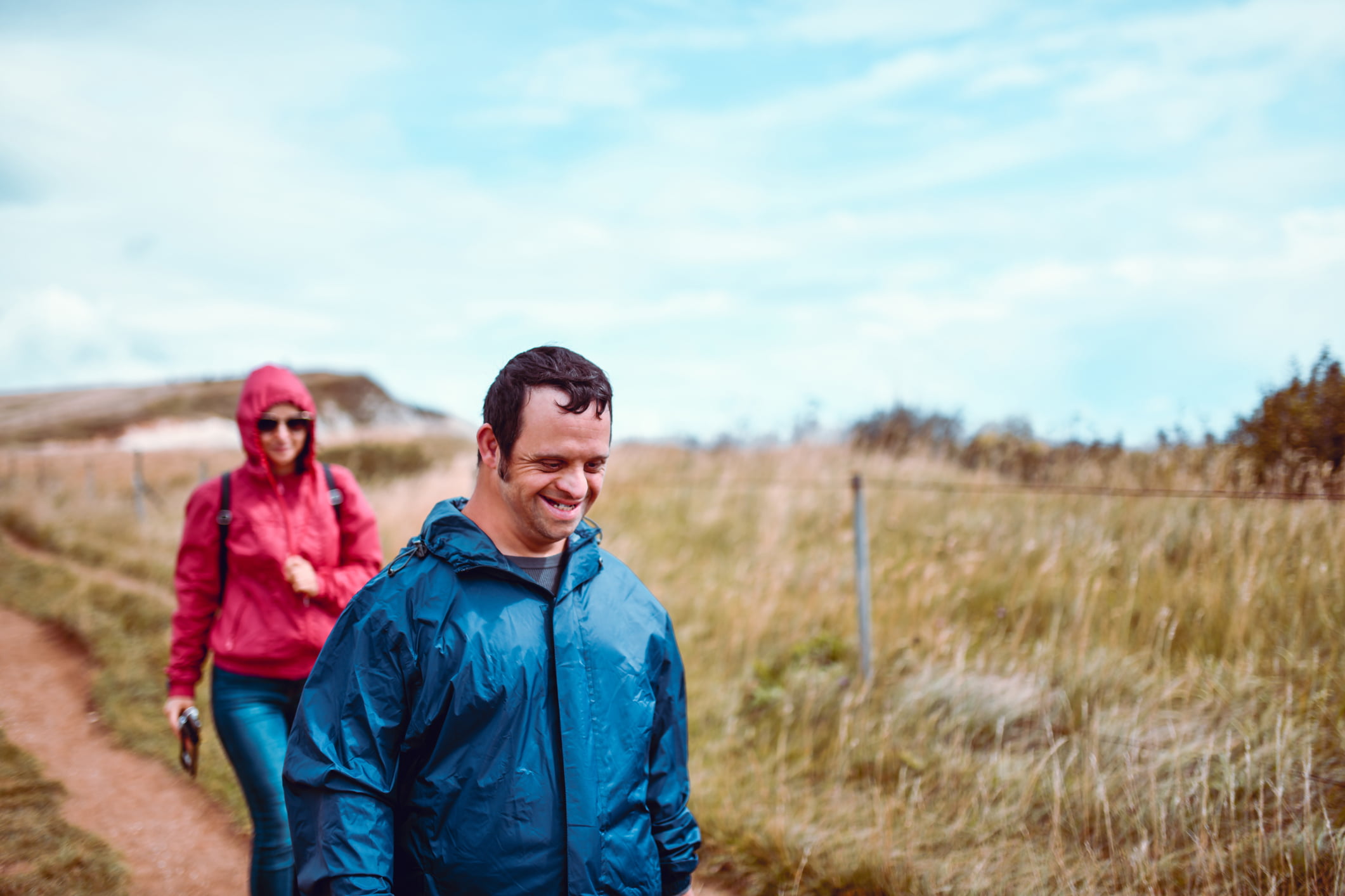 A smiling disabled man in a blue rain jacket goes for a walk with a friend.