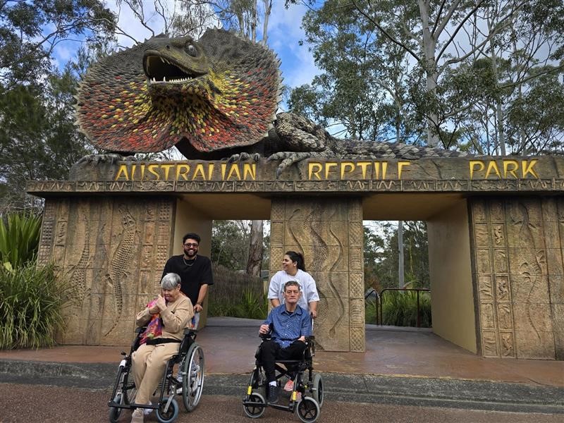 Two people in wheelchairs with their carers outside Australian Reptile Park.