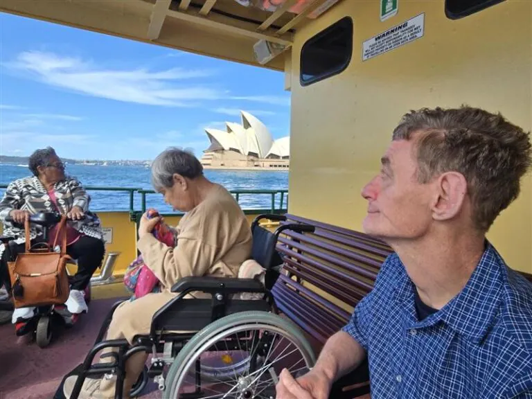 A group of people sit on a ferry, with the Sydney Opera House in view.